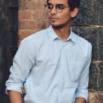 boy leaning on brick wall looking to the side in blue button-down shirt