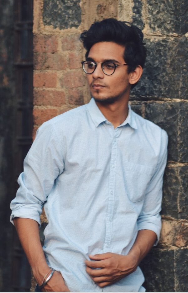 boy leaning on brick wall looking to the side in blue button-down shirt